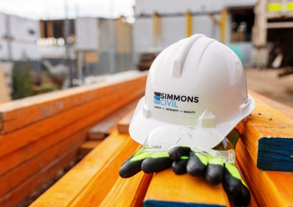 White hard hat with the Simmons Civil logo on the front sitting on a pair of work gloves