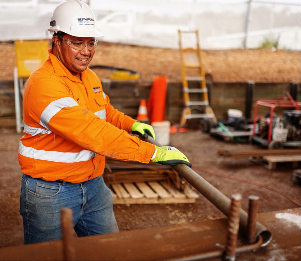 Simmons work in orange work shirt and hard hat bending a length of rebar