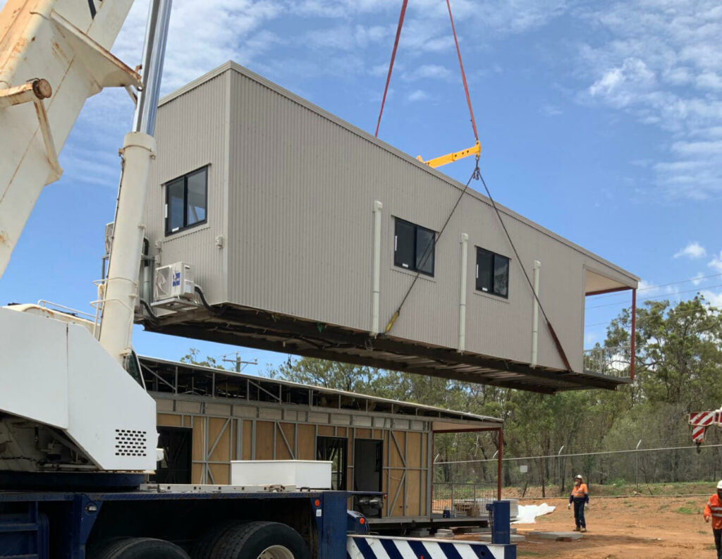 A portable building being moved by a truck crane